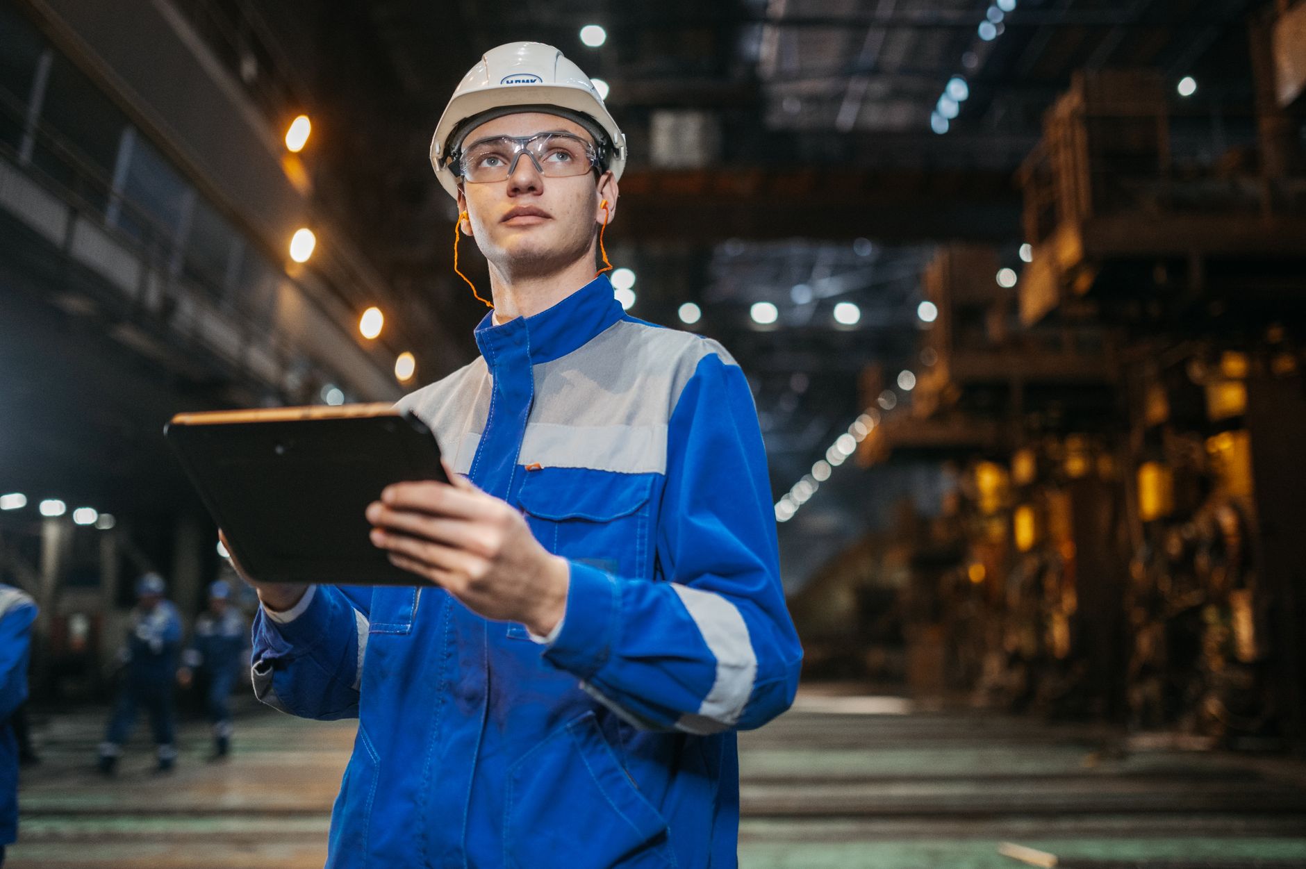 Engineer in safety gear checking data on a tablet on a factory floor